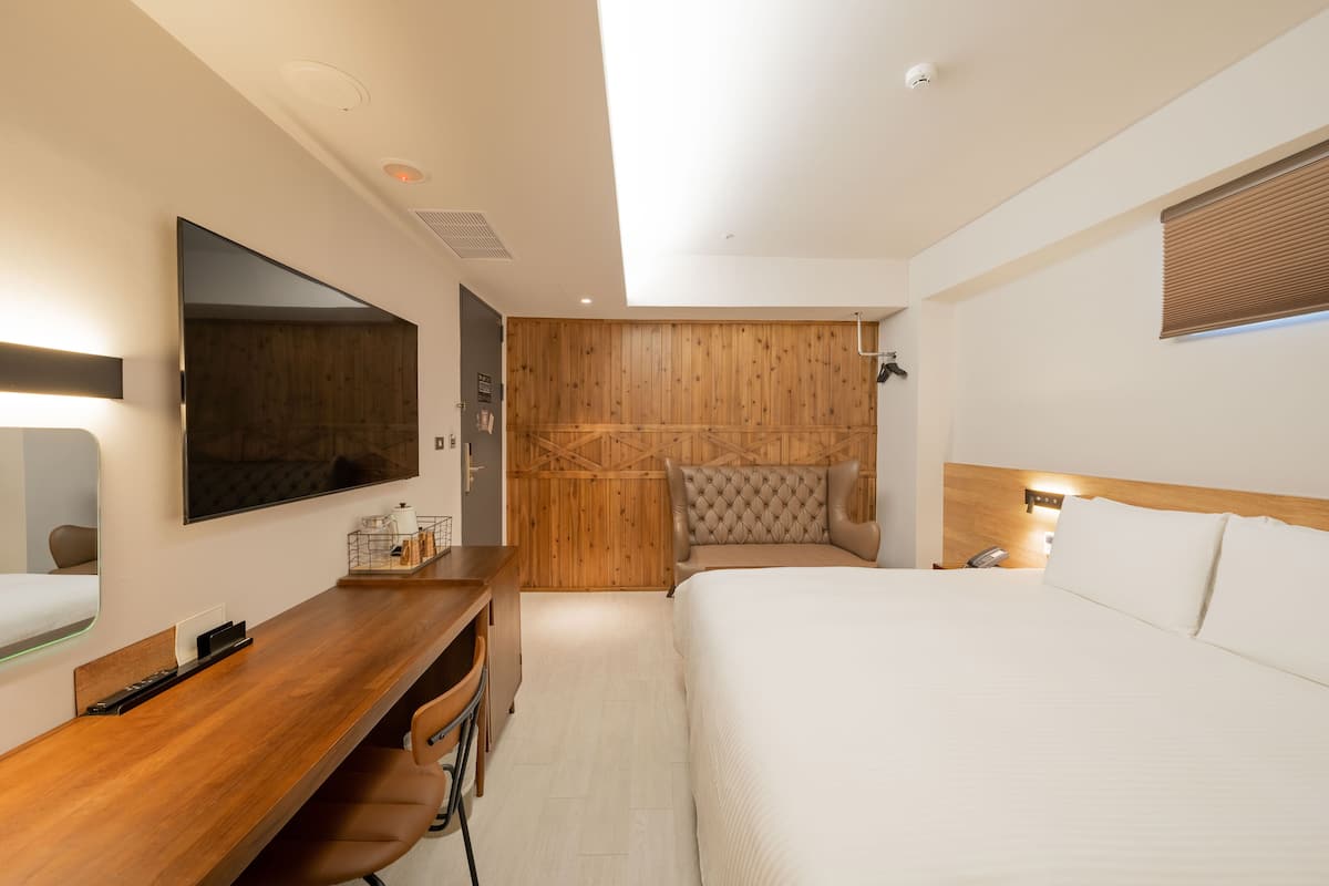 A modern hotel room with a wooden accent wall, a large bed, a desk with a chair, and a mounted TV.