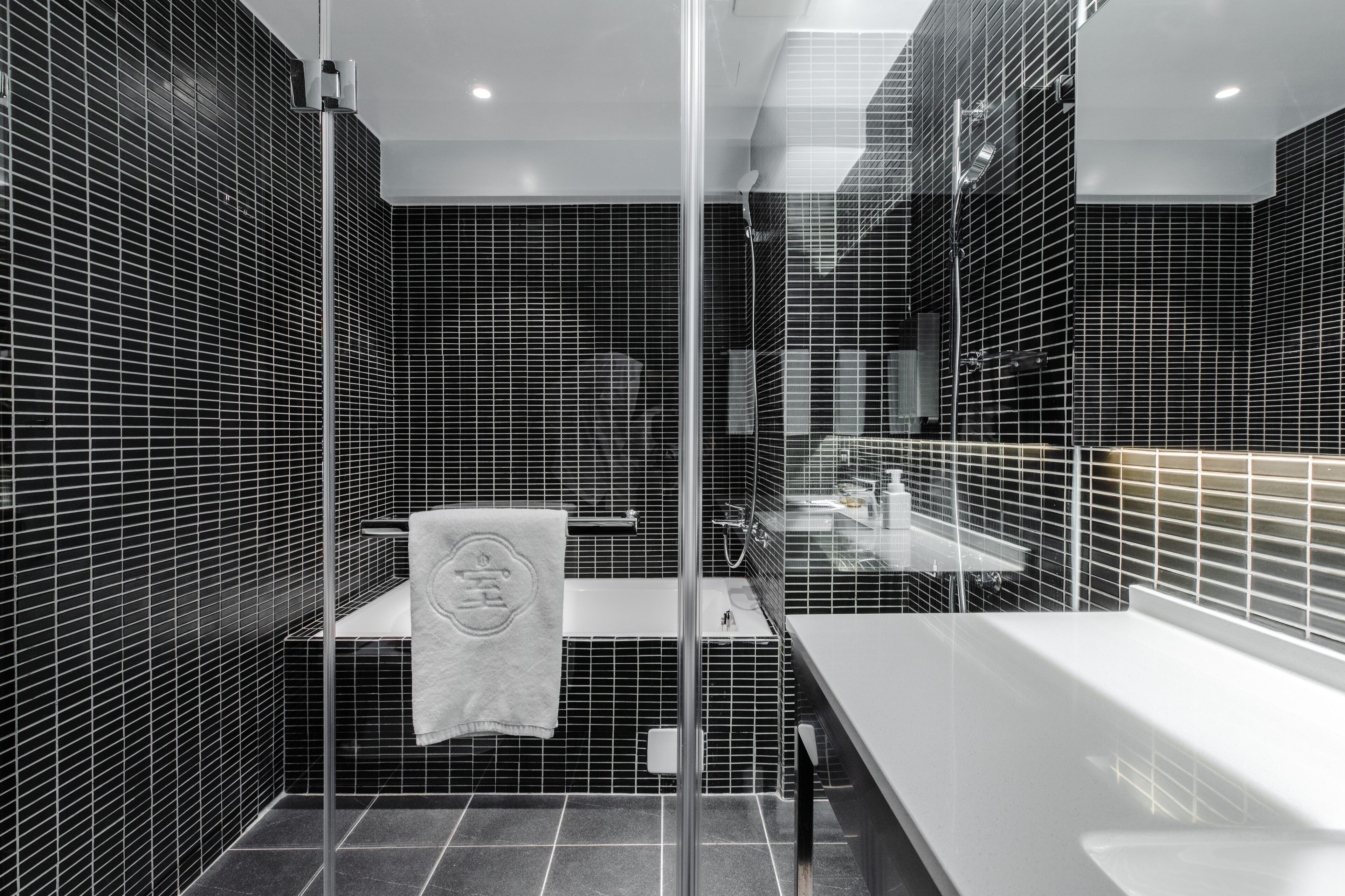 A modern bathroom with black tiled walls, a glass shower enclosure, and a white sink.