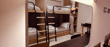 Une chambre avec un lit superposé, un grand miroir, un plancher en bois et un petit bureau avec une lampe.