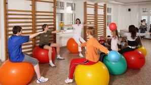 A group of people exercising on large exercise balls in a room with wooden slats on the walls and a radiator. - Lázeňská Léčebna Mánes (Karlovy Vary)