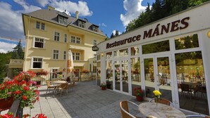 A restaurant named 'Restaurante MÁNES' with outdoor seating and a yellow building in the background. - Lázeňská Léčebna Mánes (Karlovy Vary)