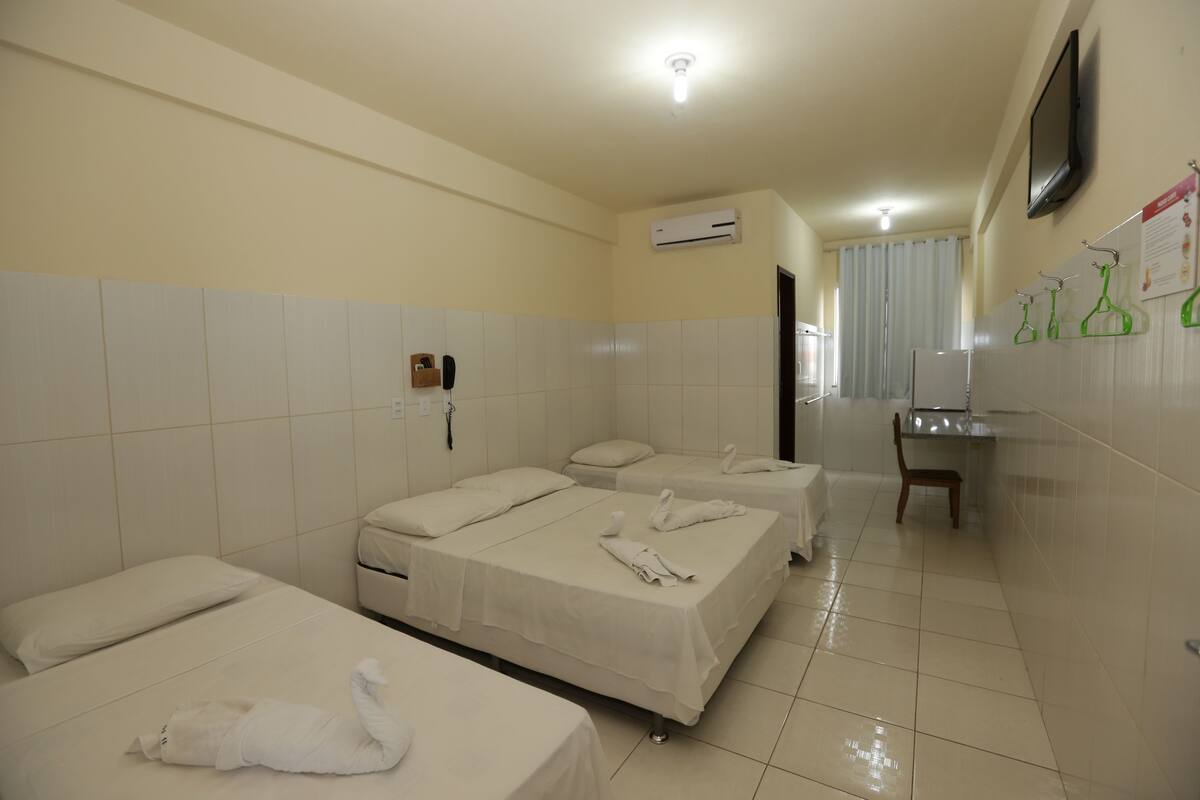 Et hotelværelse med tre enkeltsenge, et skrivebord, en stol, en klimaanlæg og et spejl på væggen.
