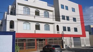 A multi-story building with a red and white facade, a car parked in front, and a blue tiled wall to the left. - Pousada Mirante das Águas (Aracaju)
