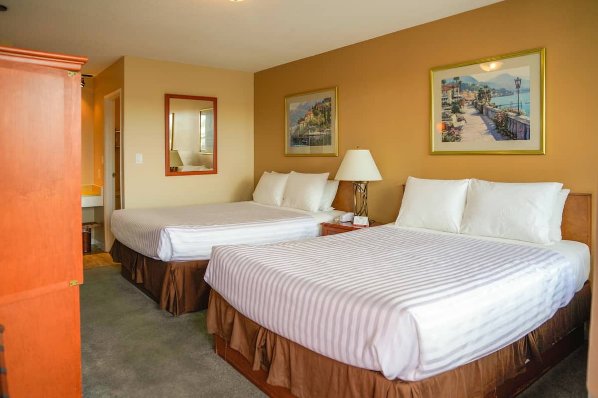 A hotel room with two beds, a mirror, and two framed pictures on the wall.
