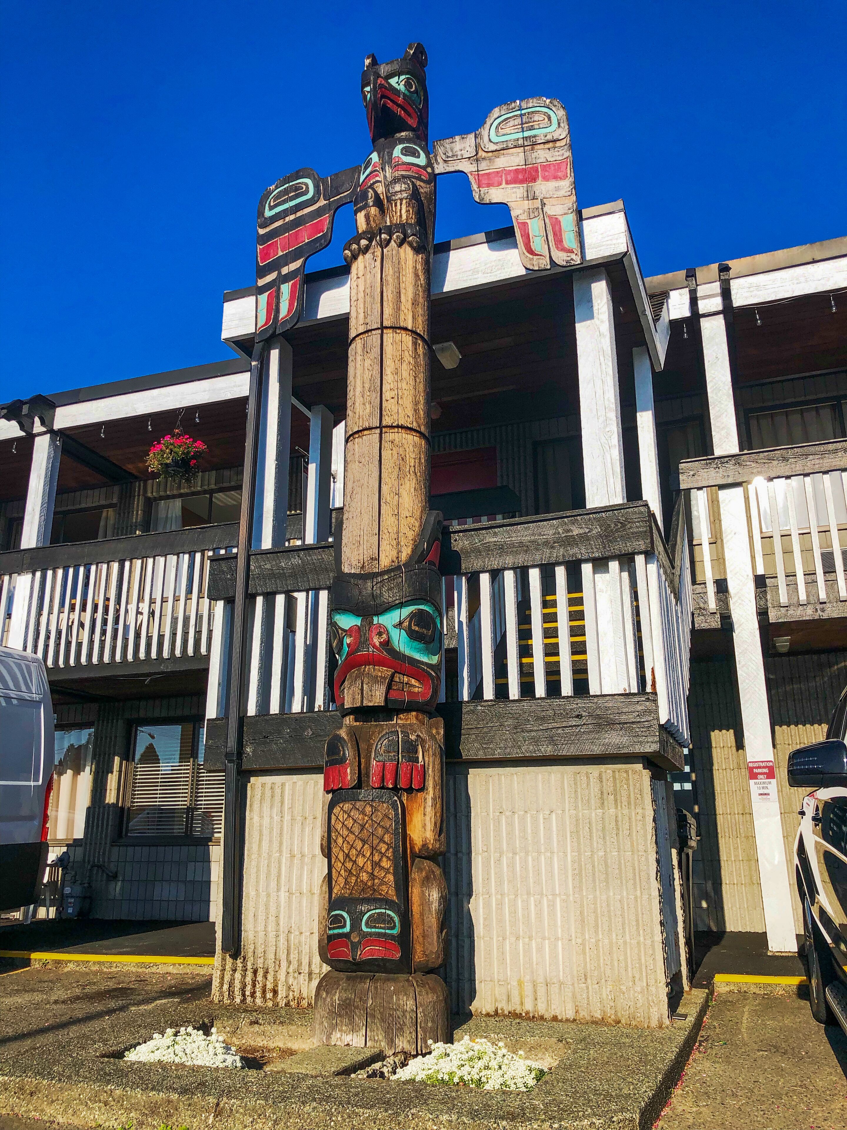 Un totem di legno di fronte a un edificio con un balcone e un'area di parcheggio.