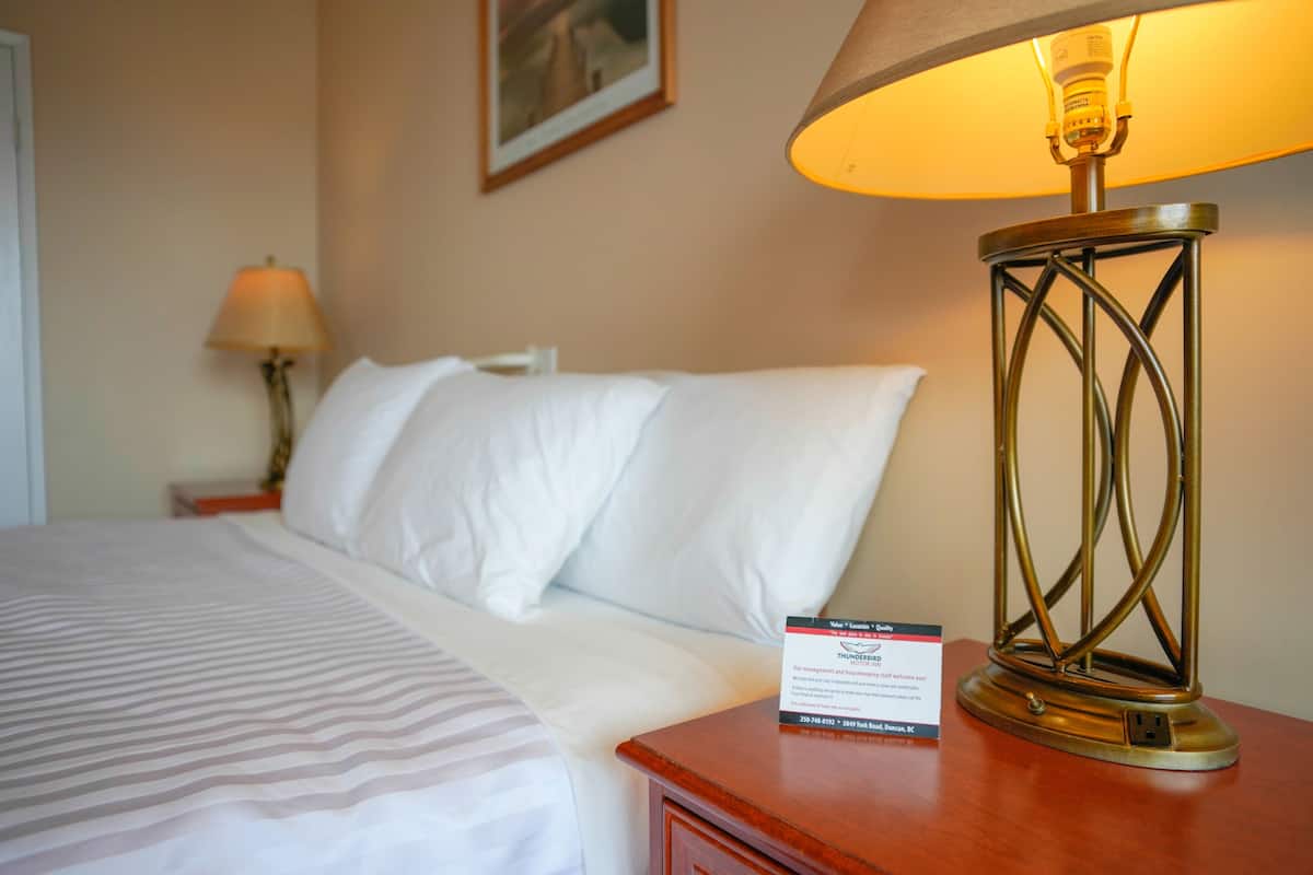 A neatly made bed with white linens, a bedside lamp, and a small card on the nightstand.
