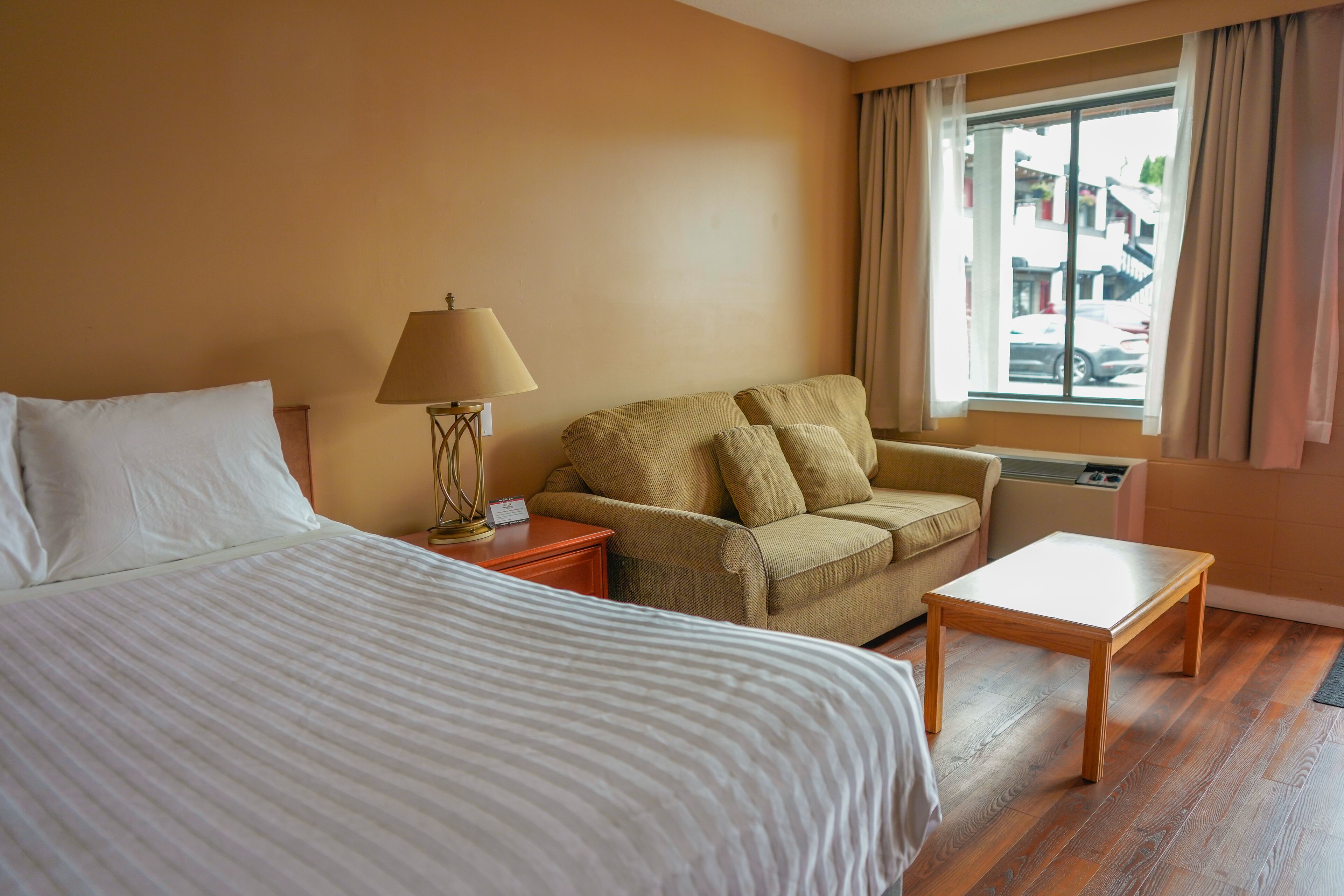 A hotel room with a bed, a sofa, a small table, and a window with curtains.