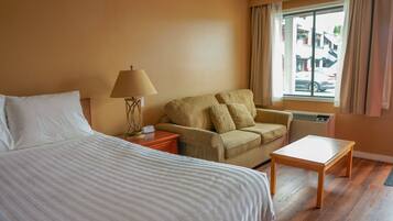 A hotel room with a bed, a sofa, a small table, and a window with curtains.
