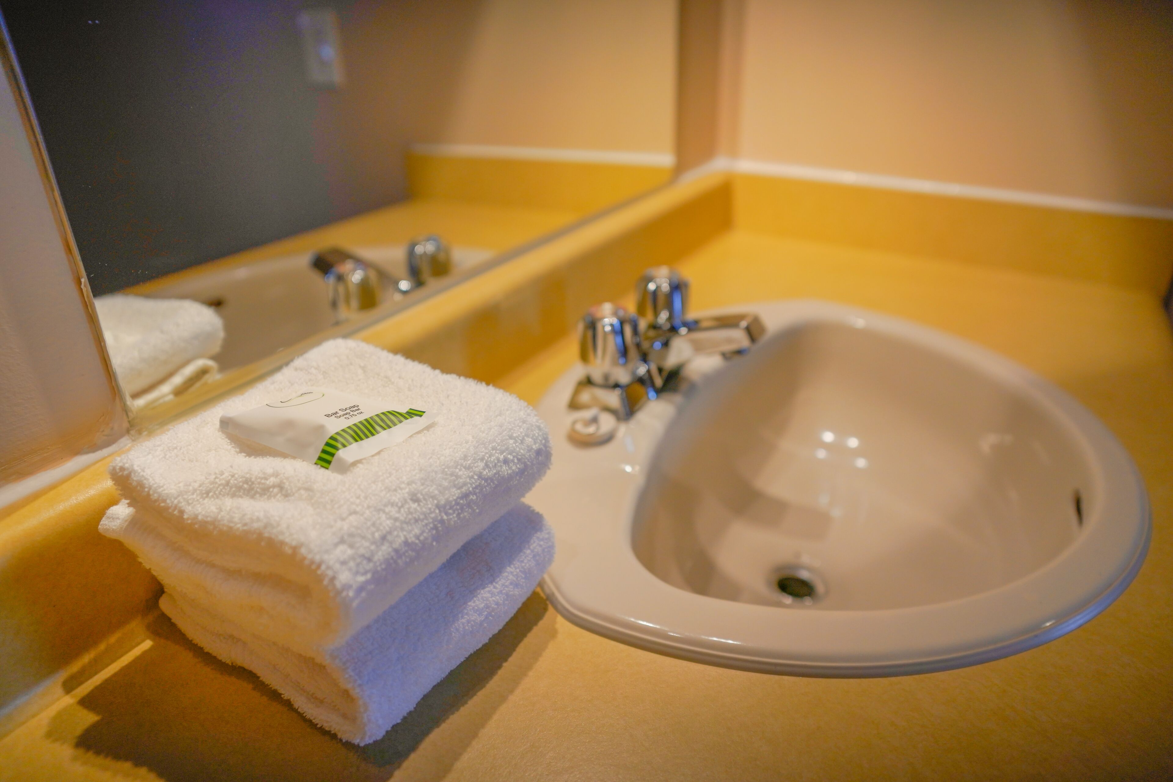 Un baño con lavamanos, espejo y toallas apiladas.