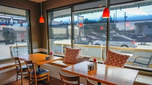 A restaurant with wooden tables and chairs, large windows with a view of the street, and hanging red pendant lights.