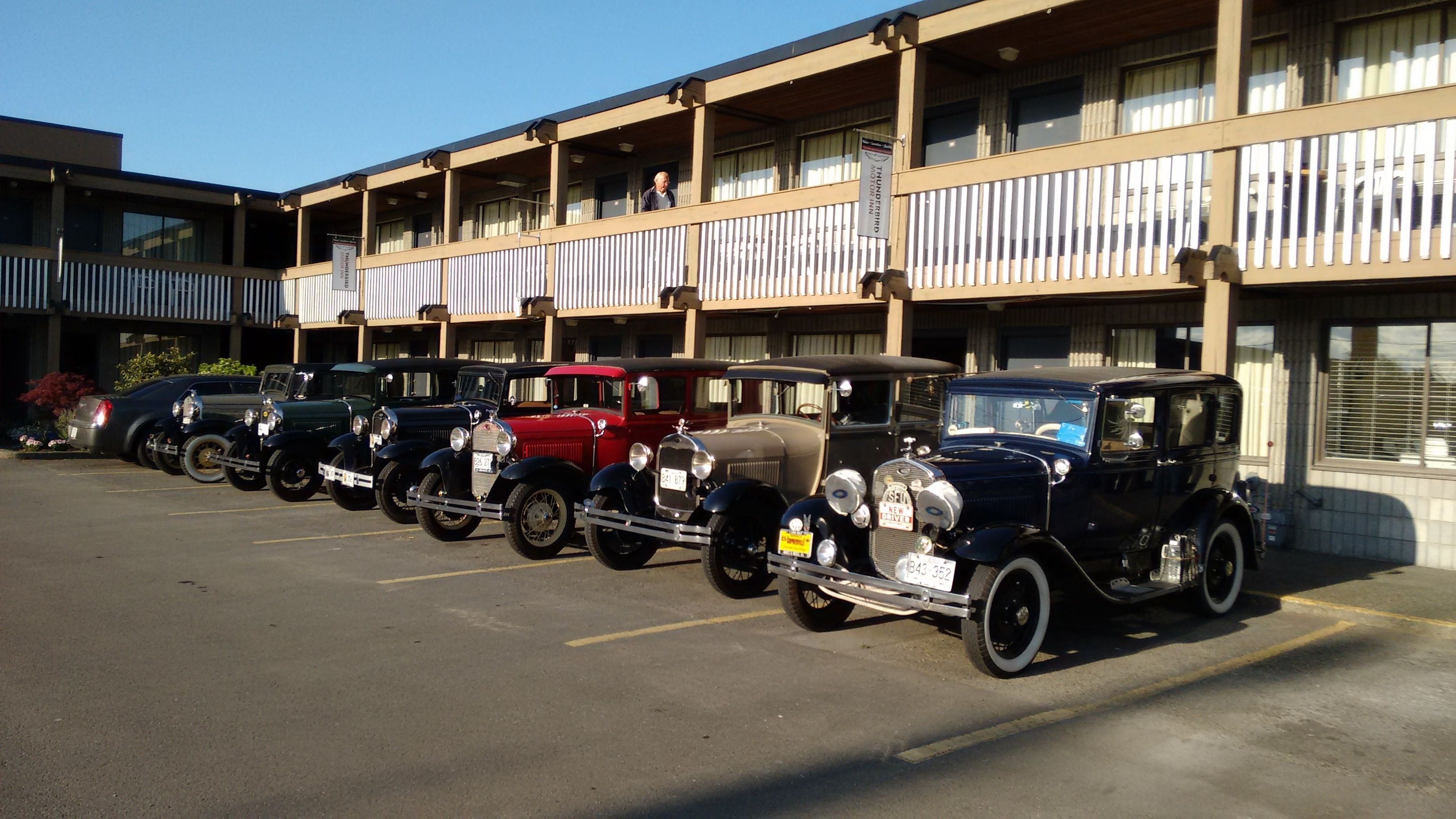 A parking lot with several vintage cars parked in front of a building with balconies.