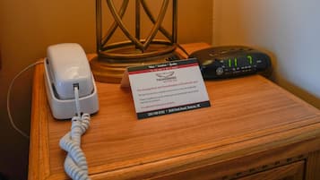 Uma mesa de cabeceira de madeira com uma lâmpada, um telefone e um relógio digital.