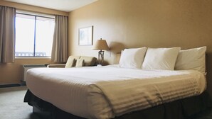 A hotel room with a large bed, a bedside table, a lamp, and a window with curtains.