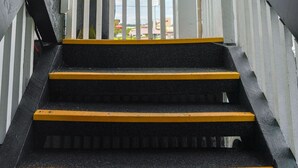 A set of outdoor stairs with a wooden handrail and white balusters, leading to a covered area.