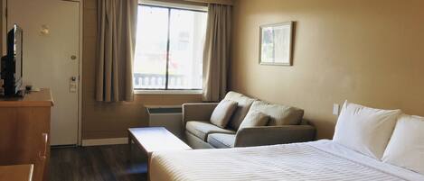 A hotel room with a bed, a sofa, a desk, and a window with curtains.