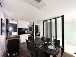 Une salle de conférence moderne dotée d’une paroi en verre, d’un téléviseur à écran plat et d’un espace repas avec une table et des chaises en marbre noir.