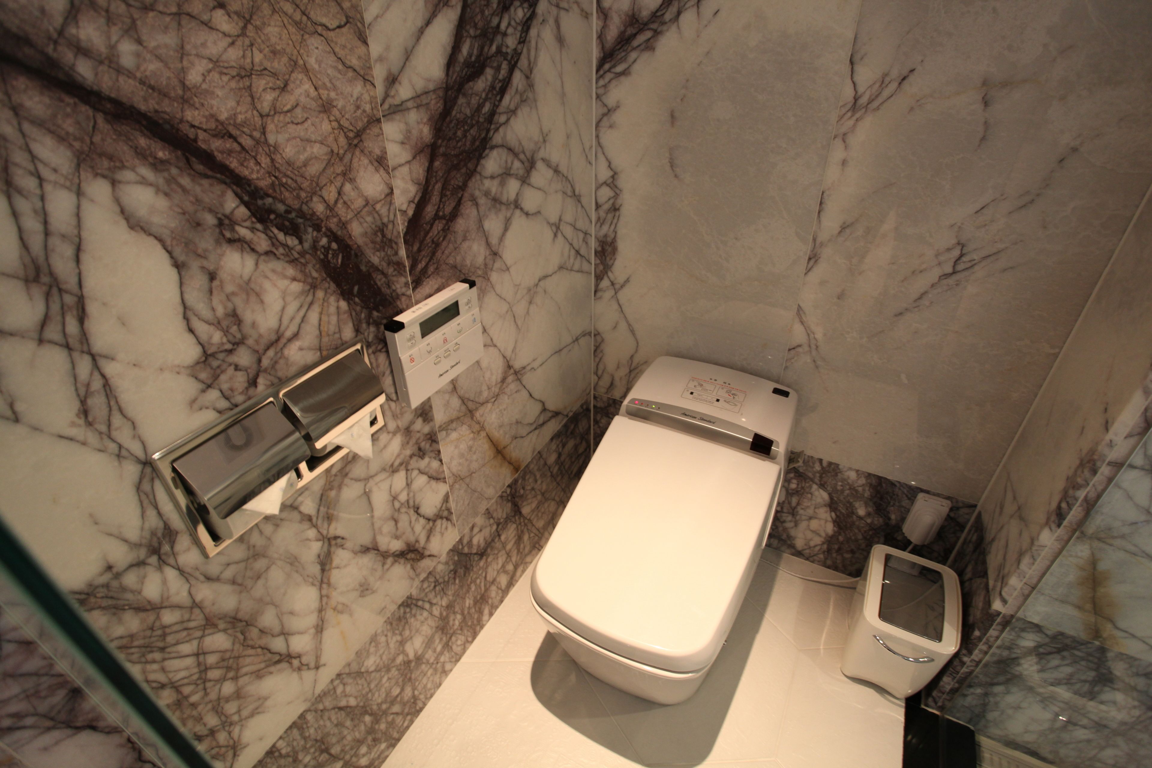 Une salle de bain moderne avec un sol et des murs en marbre, des toilettes, un bidet et une douche à parois de verre.