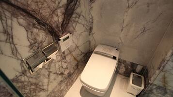 Une salle de bain moderne avec un sol et des murs en marbre, des toilettes, un bidet et une douche à parois de verre.