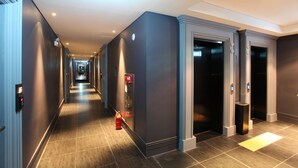 Un pasillo moderno de hotel con un largo recorrido, ascensores y un extintor.