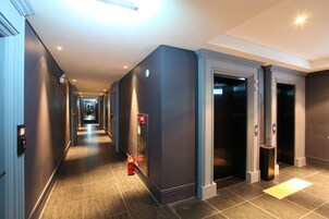 Un couloir d’hôtel moderne, avec un long passage, des ascenseurs et un extincteur.