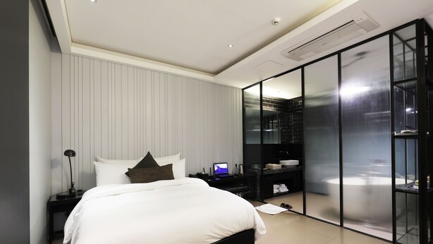 Un dormitorio moderno con una cama grande, una mesita de noche con lámpara, un televisor y un vestidor amplio con puerta de vidrio.