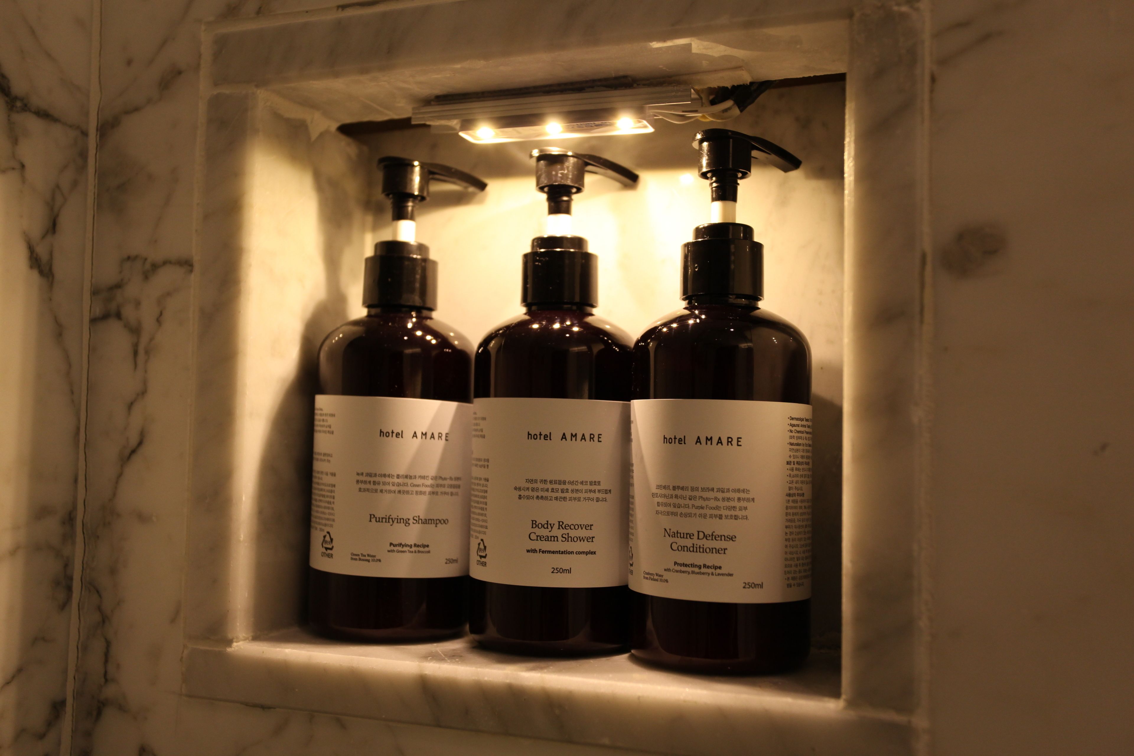 Three bottles of hotel AMARE products in a marble shelf.