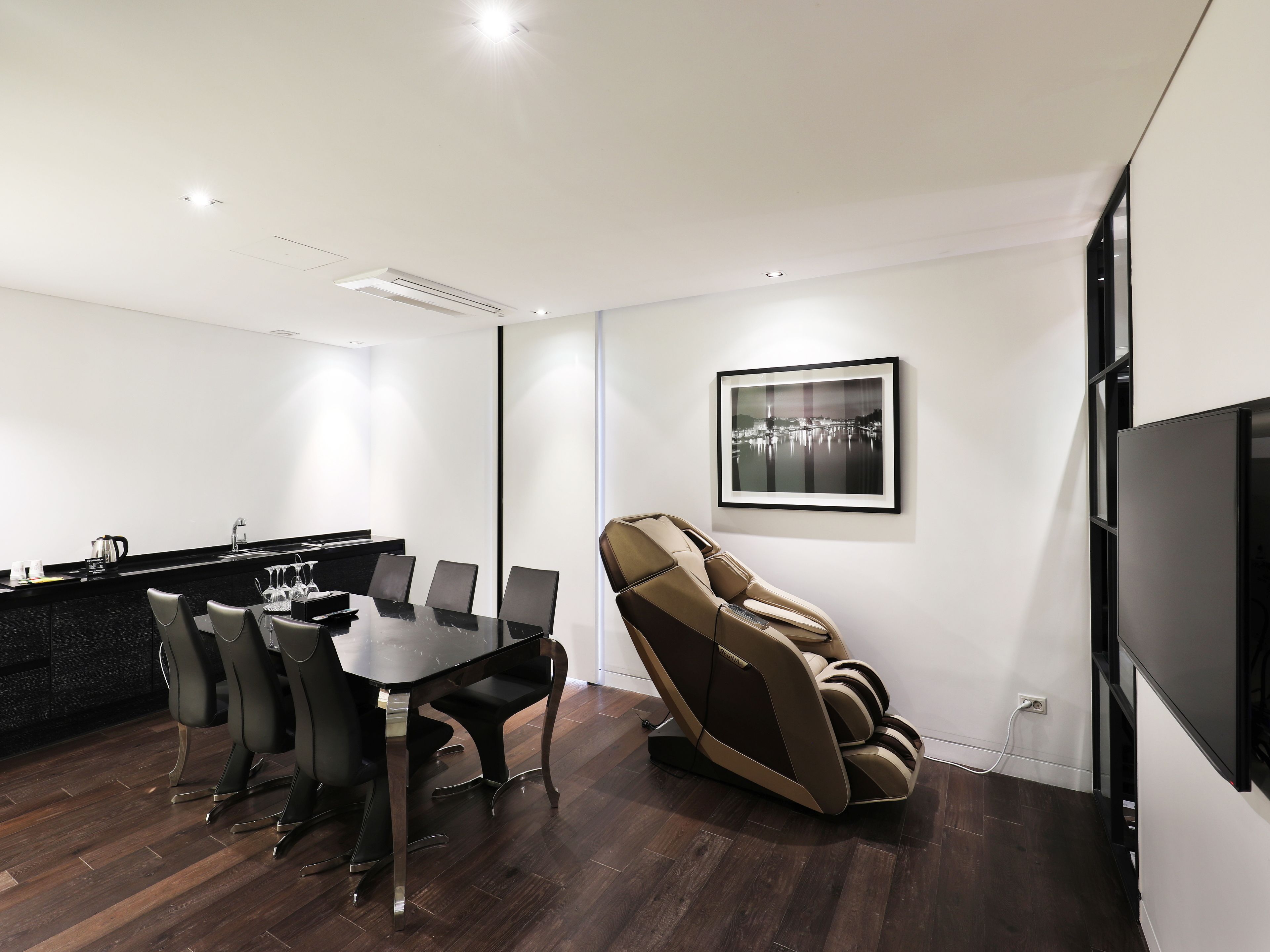 Una habitación moderna con una mesa de comedor, sillas, un sillón de masaje, un cuadro enmarcado y un televisor.