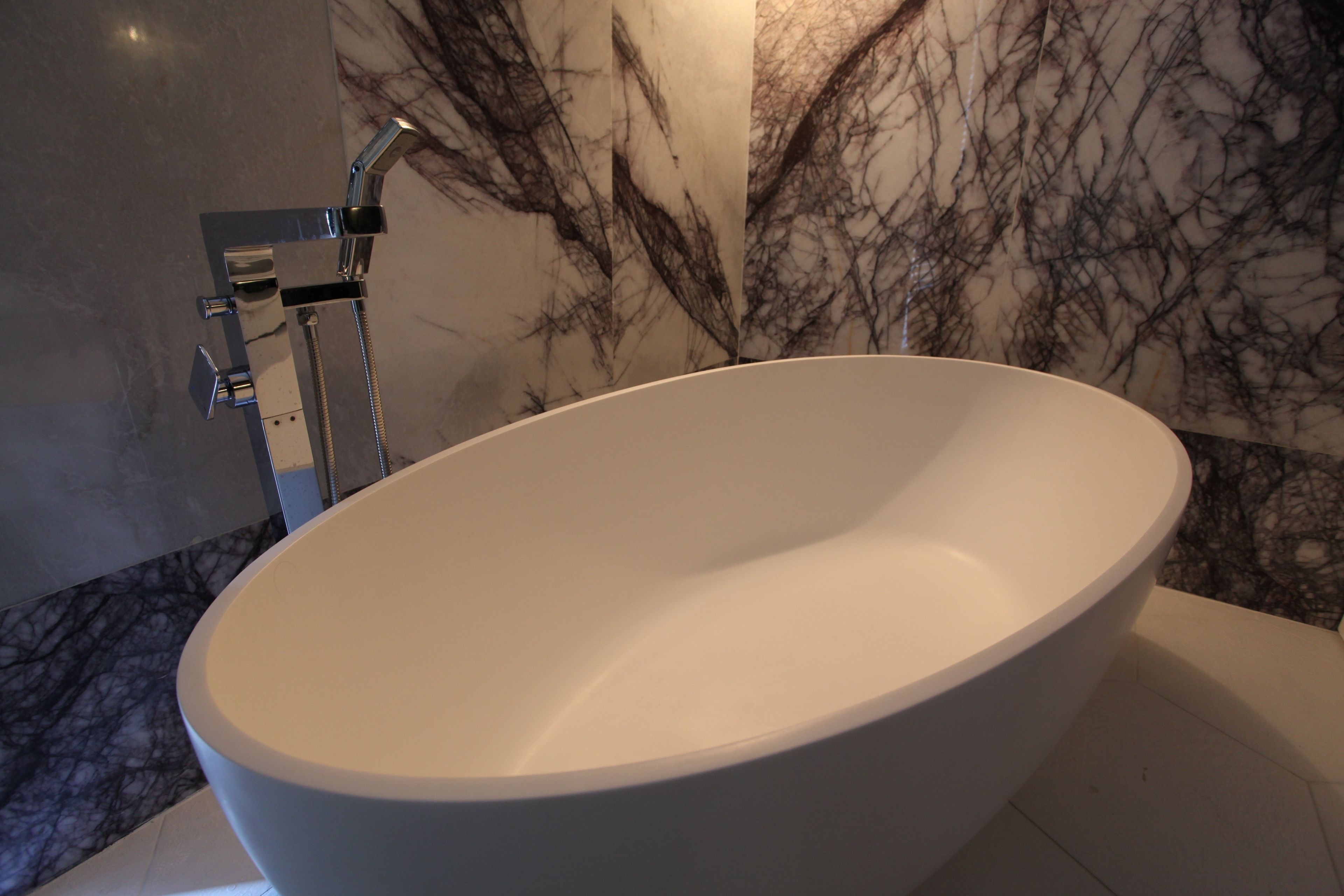 A modern bathroom with a freestanding bathtub, a chrome showerhead, and a marble wall.