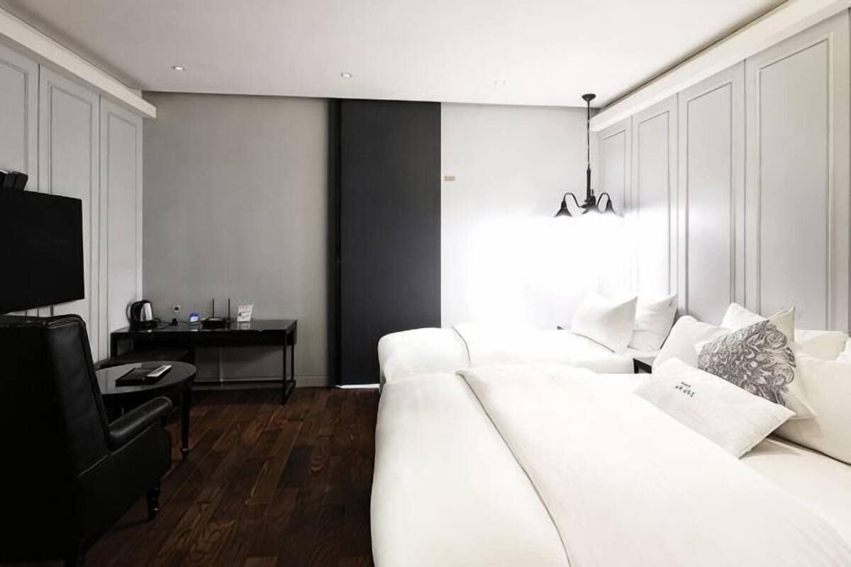 Ett modernt hotellrum med en vit säng, ett skrivbord, en tv och en kristallkrona.