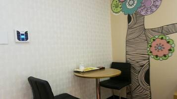 Una habitación pequeña con una mesa redonda y dos sillas. Hay un termostato instalado en la pared y un mural colorido con motivos florales.