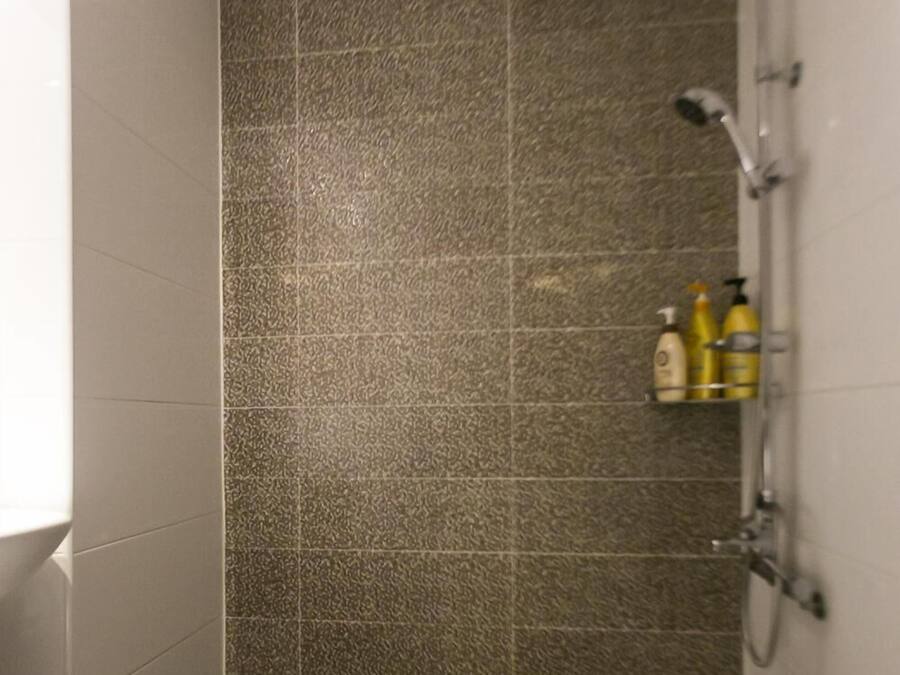 Een douchegedeelte met een zwart-wit betegelde vloer, een structuurwand en een plank met toiletartikelen.