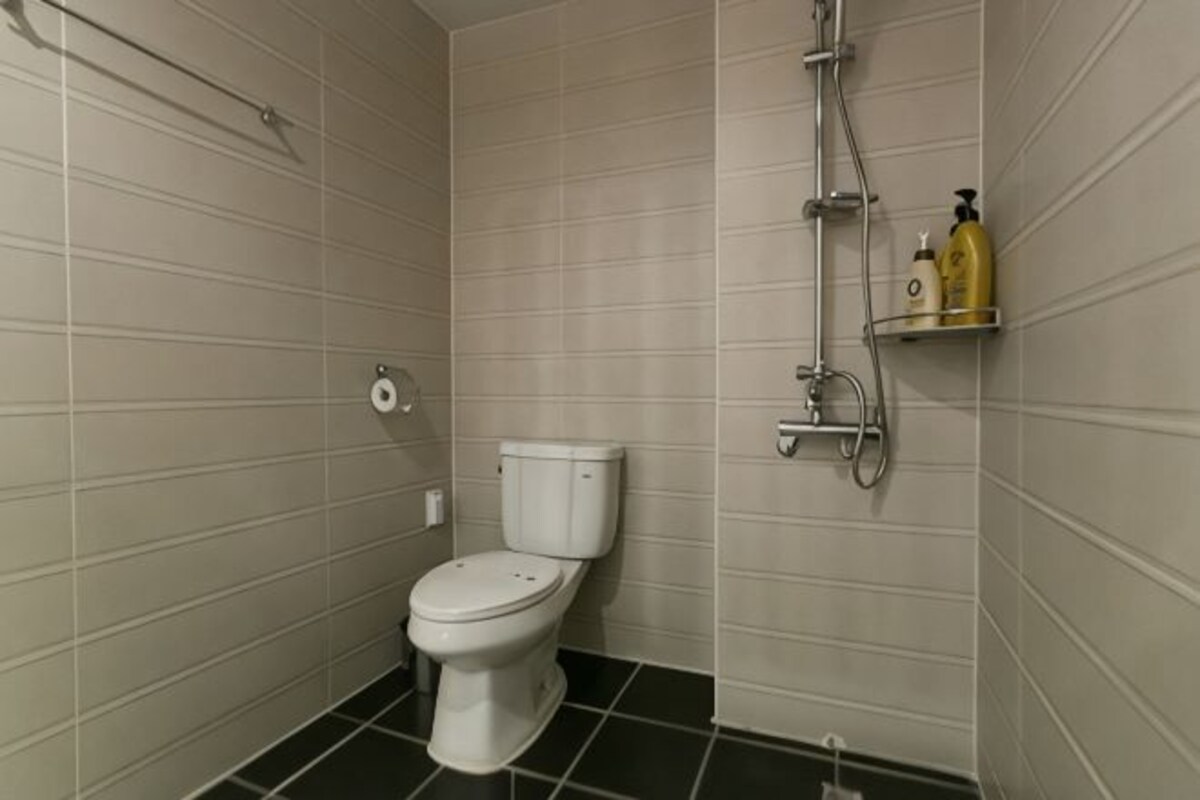 A bathroom with a toilet, a shower, and a shelf with toiletries.