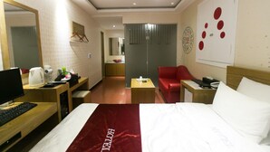 Une chambre d’hôtel avec un lit, un bureau avec un ordinateur, une chaise rouge, une petite table et un miroir.