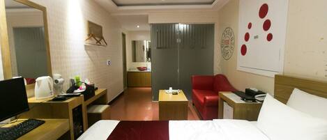Een hotelkamer met een bed, een bureau met een computer, een rode stoel, een kleine tafel en een spiegel.