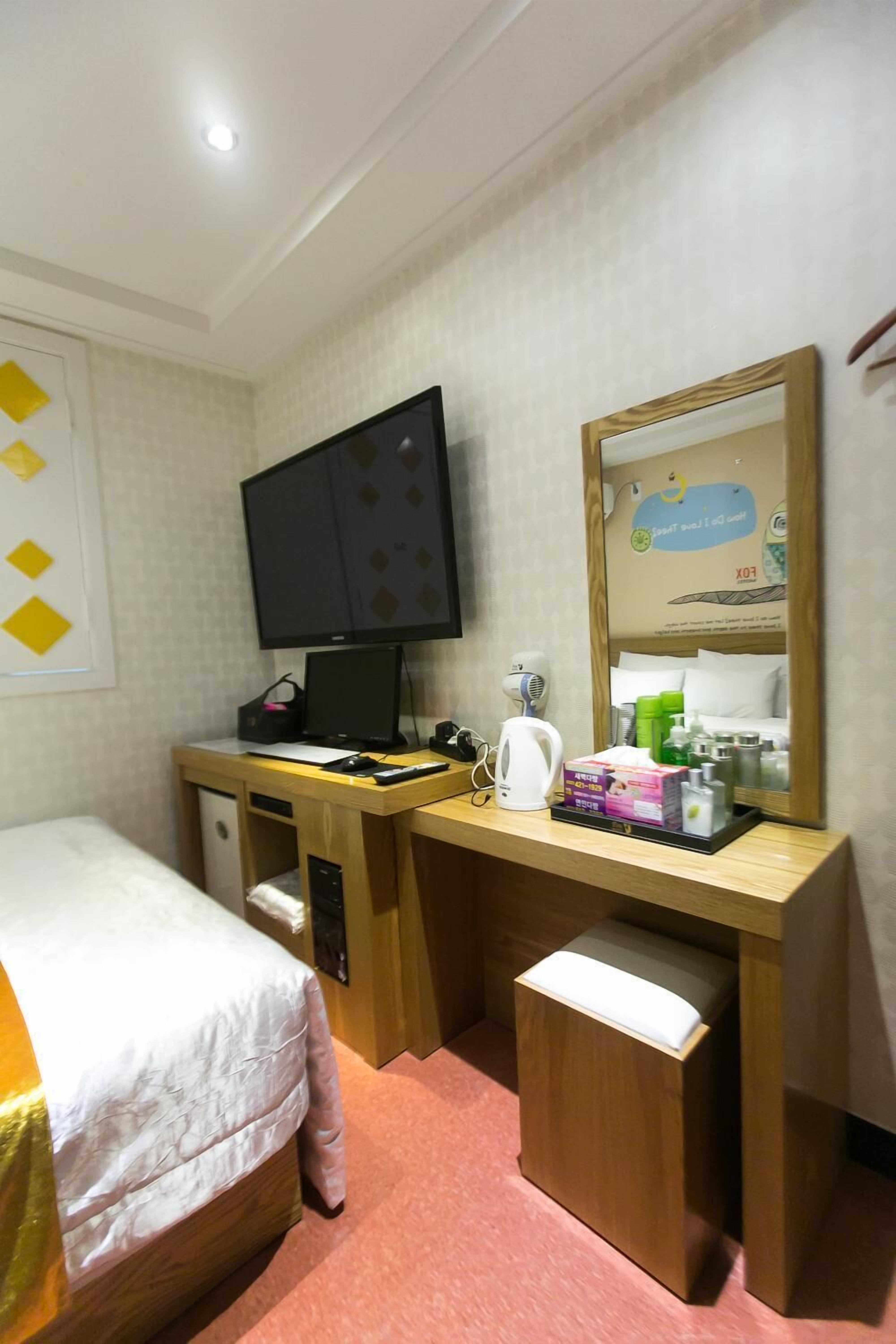 A hotel room with a bed, a desk with a computer, a mirror, and a small seating area.