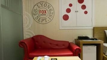 A room with a red sofa, a wooden table, a small desk with a printer, and a wall with a circular logo and red circles.