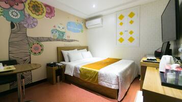 A hotel room with a bed, a desk, a chair, a table, and a wall with colorful decorations.