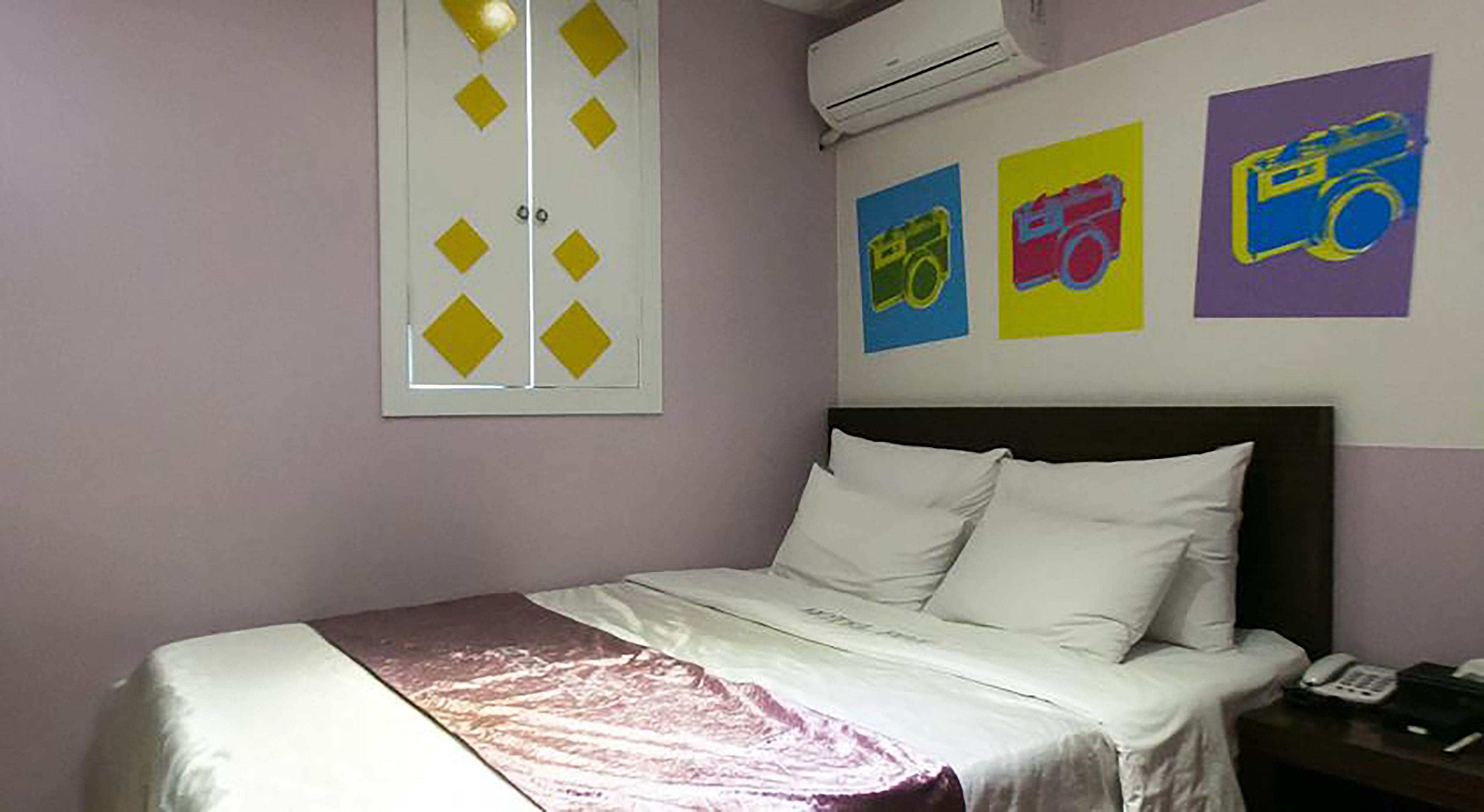 Una camera da letto con un letto, un comodino e una parete con tre poster colorati.