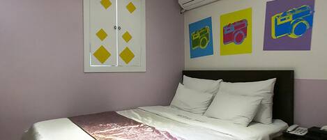 A bedroom with a bed, a nightstand, and a wall with three colorful posters.