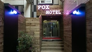 Un couloir au plancher de bois menant à l'entrée d'un motel, avec une enseigne au néon.