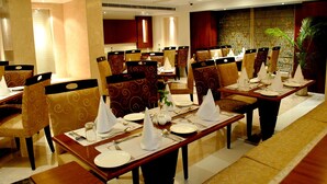 A restaurant with tables set for dining, chairs with patterned upholstery, and a decorative wall with a plant. - Hotel Libra (Jaipur)