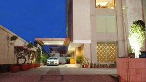 A modern building with a car parked in front, potted plants, and a well-lit entrance. - Hotel Libra (Jaipur)