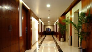 A hotel corridor with wooden doors, a marble floor, and potted plants. - Hotel Libra (Jaipur)