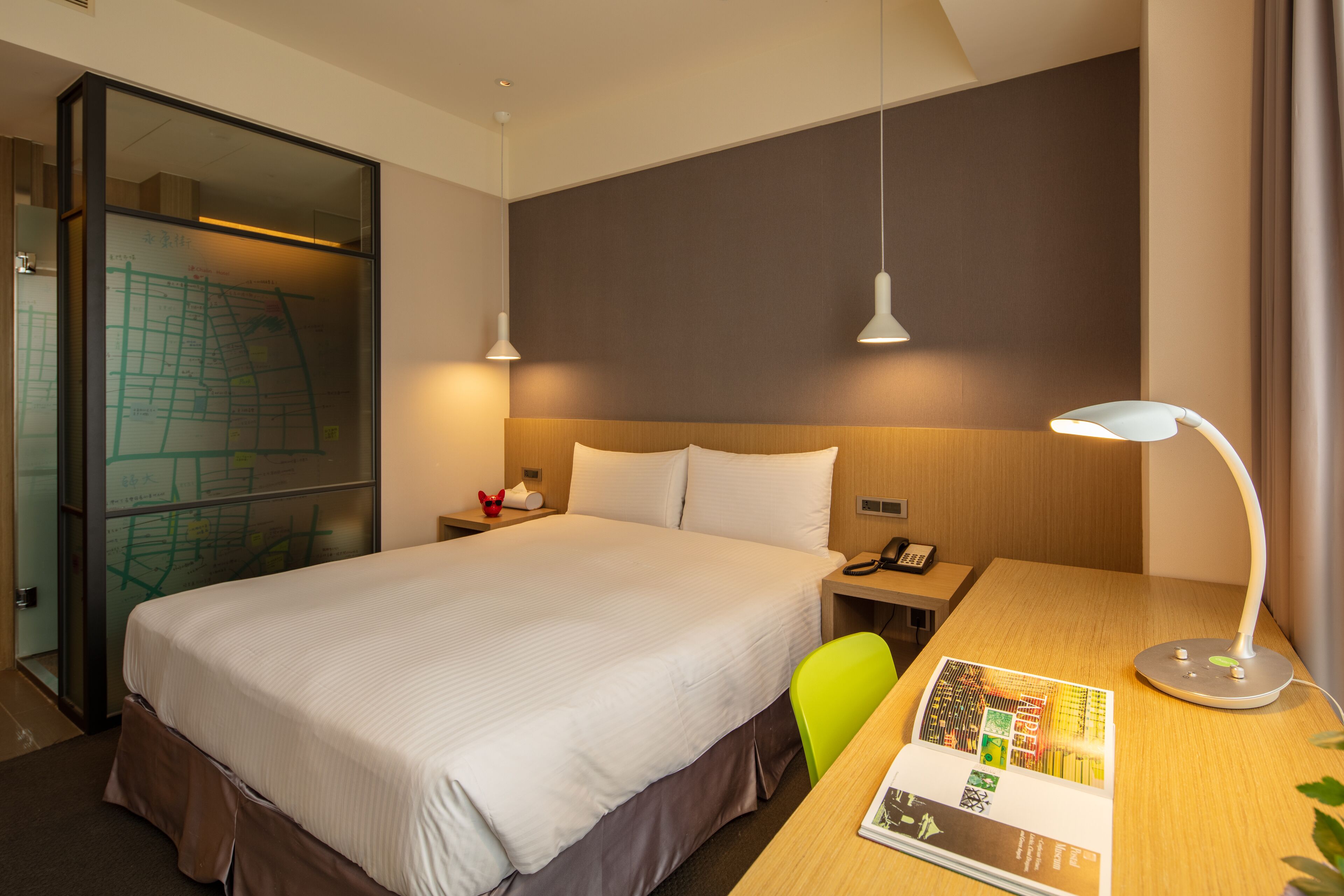 Una camera d'albergo con un letto grande, una scrivania con una lampada, una sedia e una mappa appesa al muro.