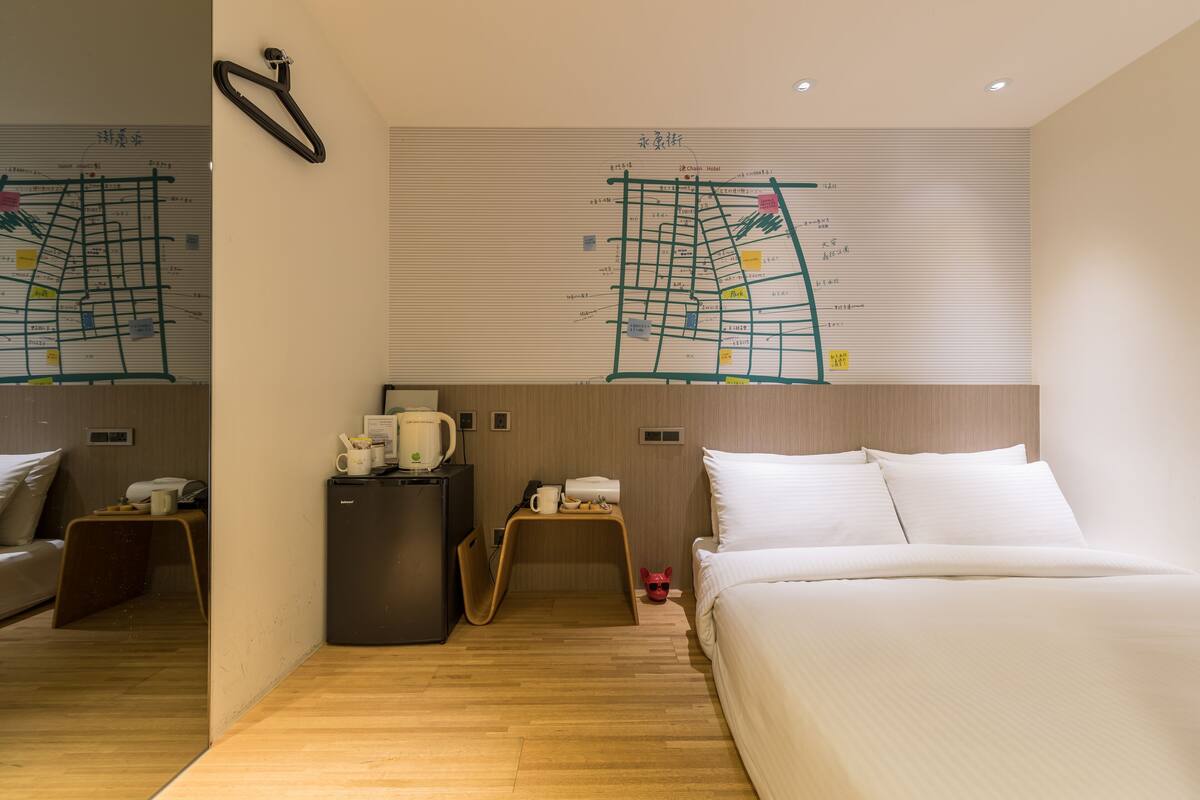 Quarto de hotel com cama, escrivaninha, frigorífico, máquina de café e um mapa na parede.
