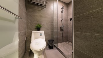 Casa de banho moderna com sanita, uma pequena planta, um cesto de lixo e zona de duche.