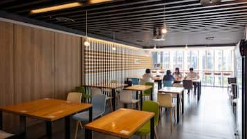 A modern restaurant with wooden tables and chairs, a striped ceiling, and large windows offering a city view.
