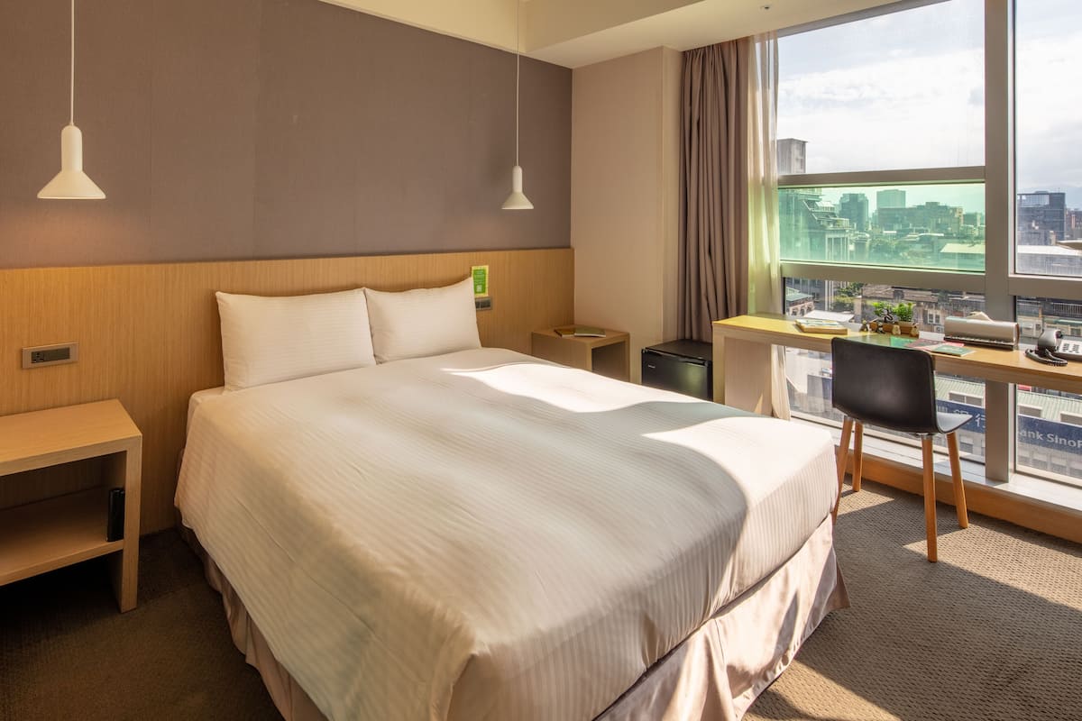 Quarto de hotel com uma cama grande, uma escrivaninha e vista para a cidade.