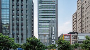 Een modern hoog gebouw met meerdere verdiepingen en balkons, omgeven door andere gebouwen en bomen.