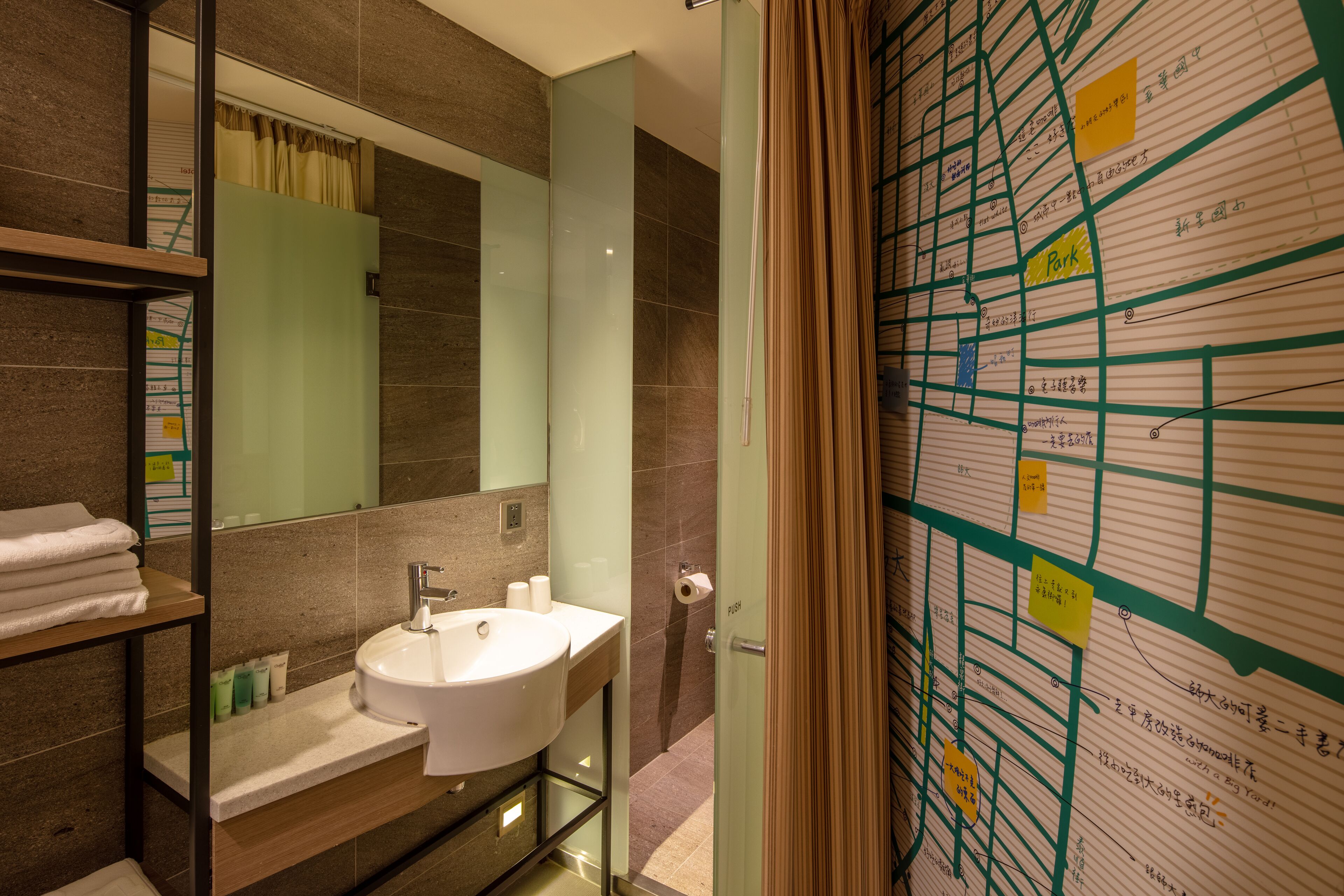 Un bany modern amb un mirall gran, un lavabo i una zona de dutxa. Hi ha tovalloles a una estant i un mapa a la paret.